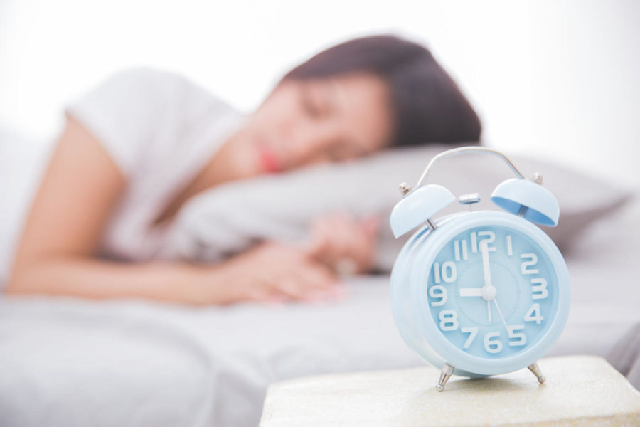48377023 - alarm clock close up with woman sleeping peacefully on a bed on the back