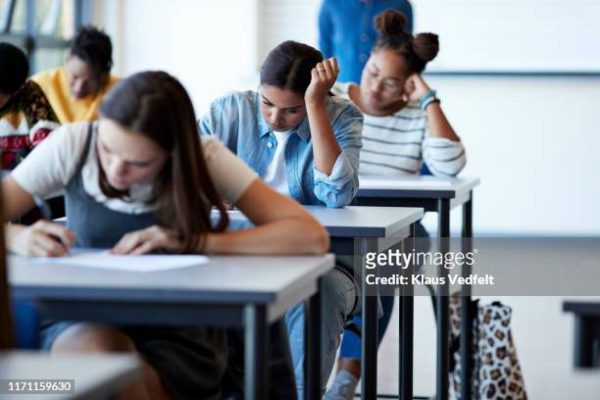 Young multi-ethnic female university students writing on papers at desks during exams in community college classroom